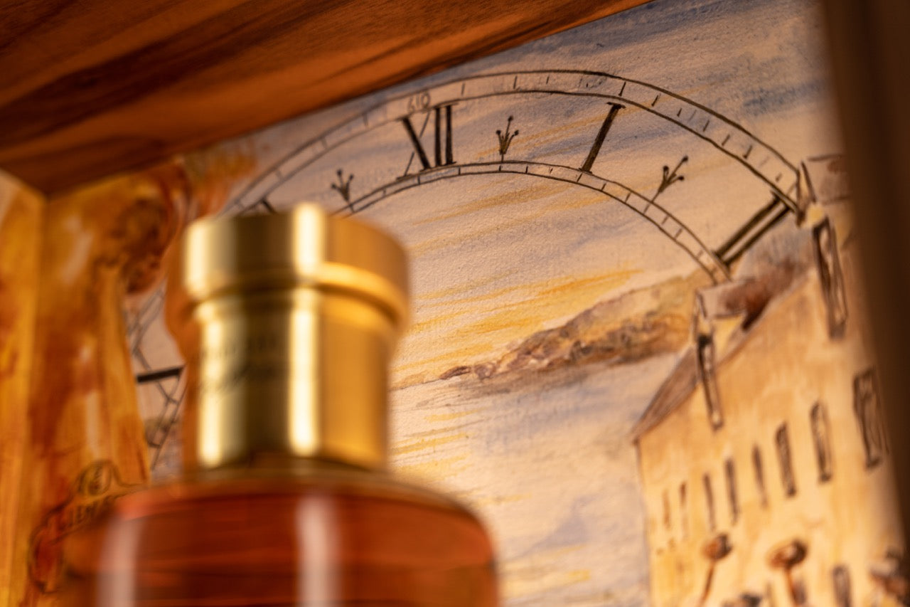 A close-up image features a bottle of liquor in the foreground with a detailed drawing in the background. The artwork depicts a large clock with Roman numerals and a scenic view of buildings and a body of water under a sunset sky.