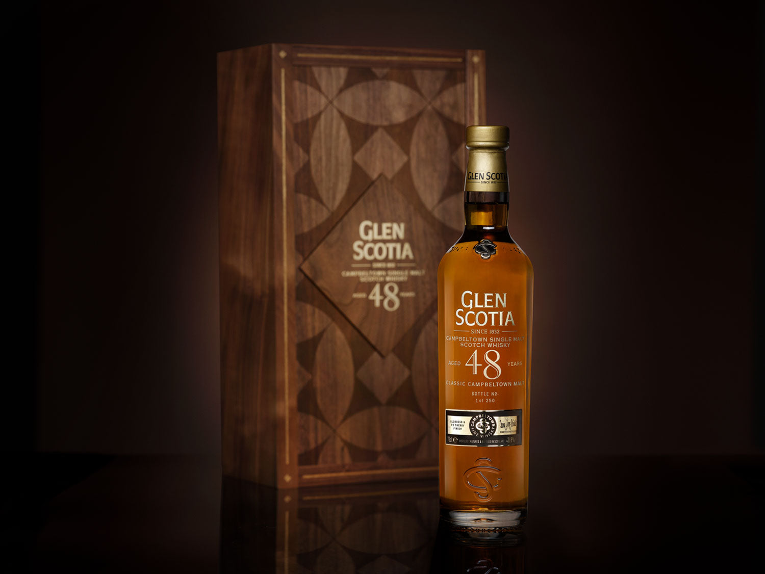 A Glen Scotia 48-year-old single malt Scotch whisky bottle is displayed against a dark background. The label reads "Glen Scotia" and "48." Behind the bottle, there is an elegant wooden box featuring the Glen Scotia logo and intricate geometric patterns.