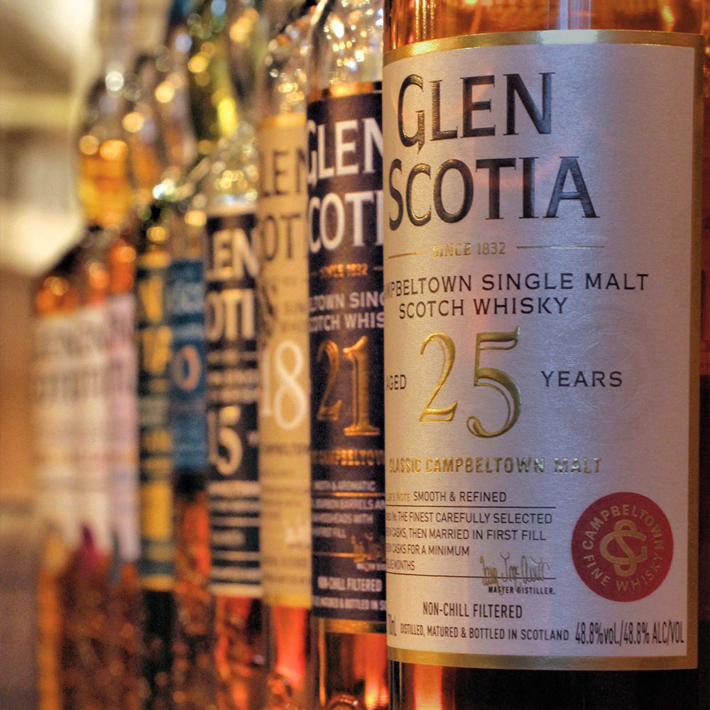 Close-up view of several bottles of Glen Scotia Campbeltown Single Malt Scotch Whisky, showcasing a 25-year aged variety in the foreground. The labels highlight key details about the whisky, including age, distillation information, and alcohol content.