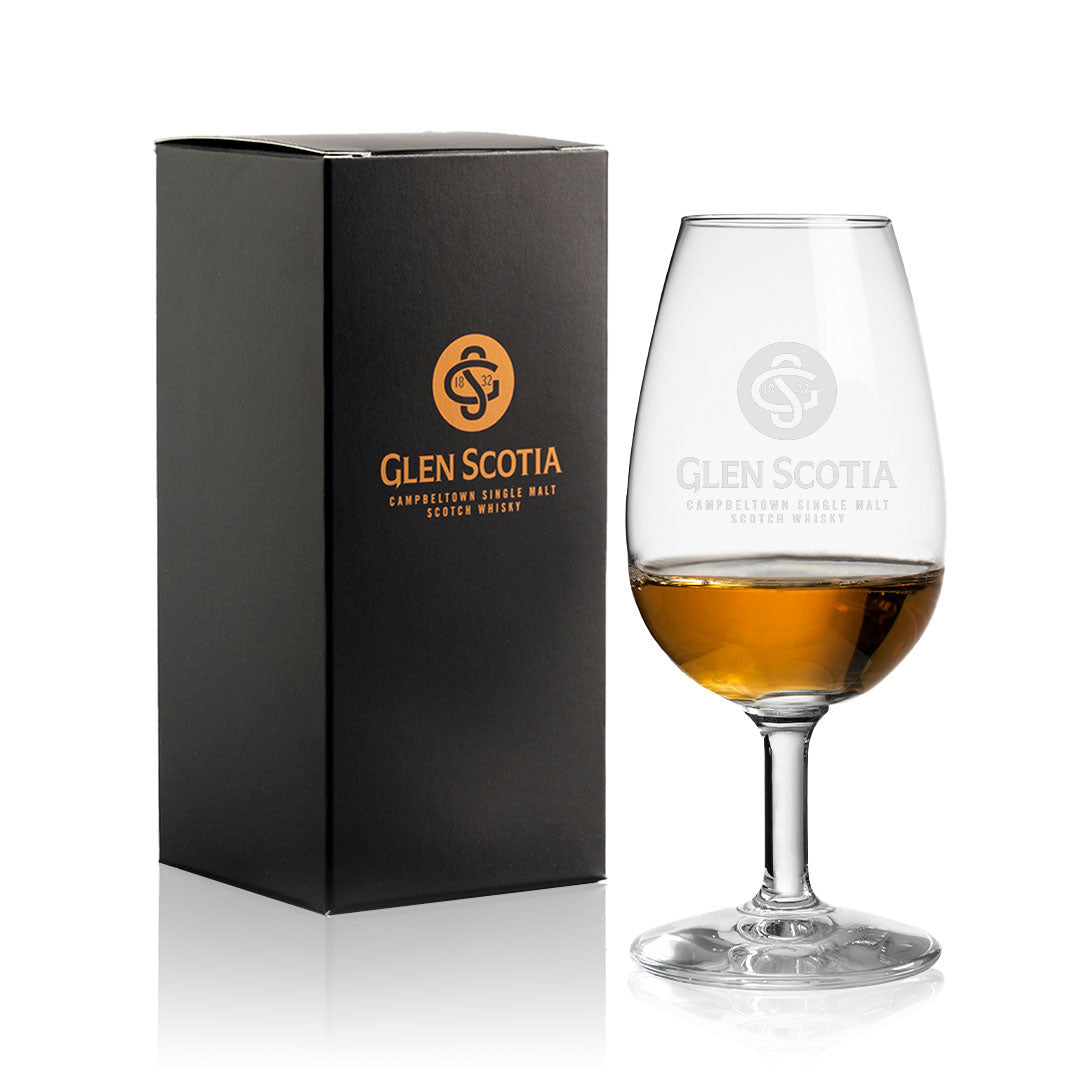 A branded black box featuring the "Glen Scotia" text and logo in gold is displayed beside a partially filled Glencairn Copita with the Glen Scotia Logo. The glass, also adorned with the "Glen Scotia" logo and text, highlights the elegance of Single Malt Scotch. This amber-colored liquid makes a perfect choice for whisky gifts.