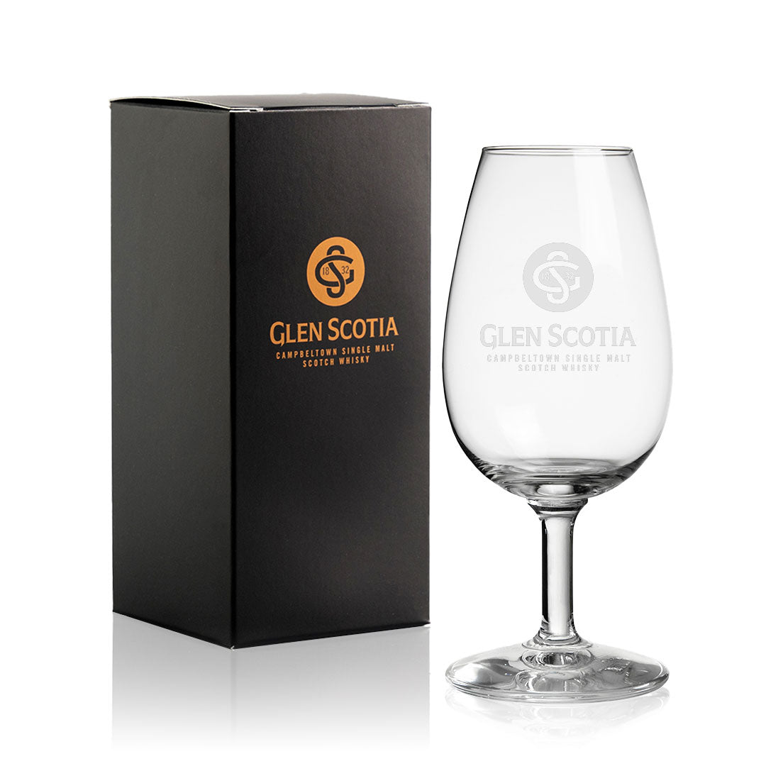 A branded black box featuring the "Glen Scotia" text and logo in gold is displayed beside a partially filled Glencairn Copita with the Glen Scotia Logo. The glass, also adorned with the "Glen Scotia" logo and text, highlights the elegance of Single Malt Scotch. This amber-colored liquid makes a perfect choice for whisky gifts.