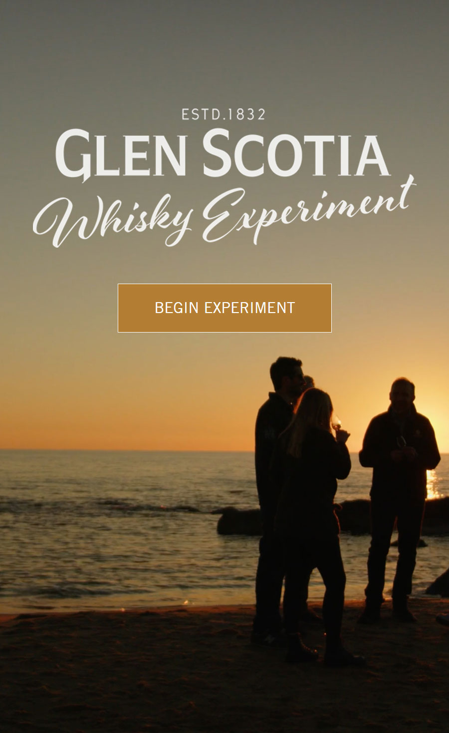 A beach scene at sunset with three silhouetted individuals holding glasses. Text above them reads, "ESTD. 1832 Glen Scotia Whisky Experiment" with a button below saying "Begin Experiment." The ocean and the setting sun create a serene background.