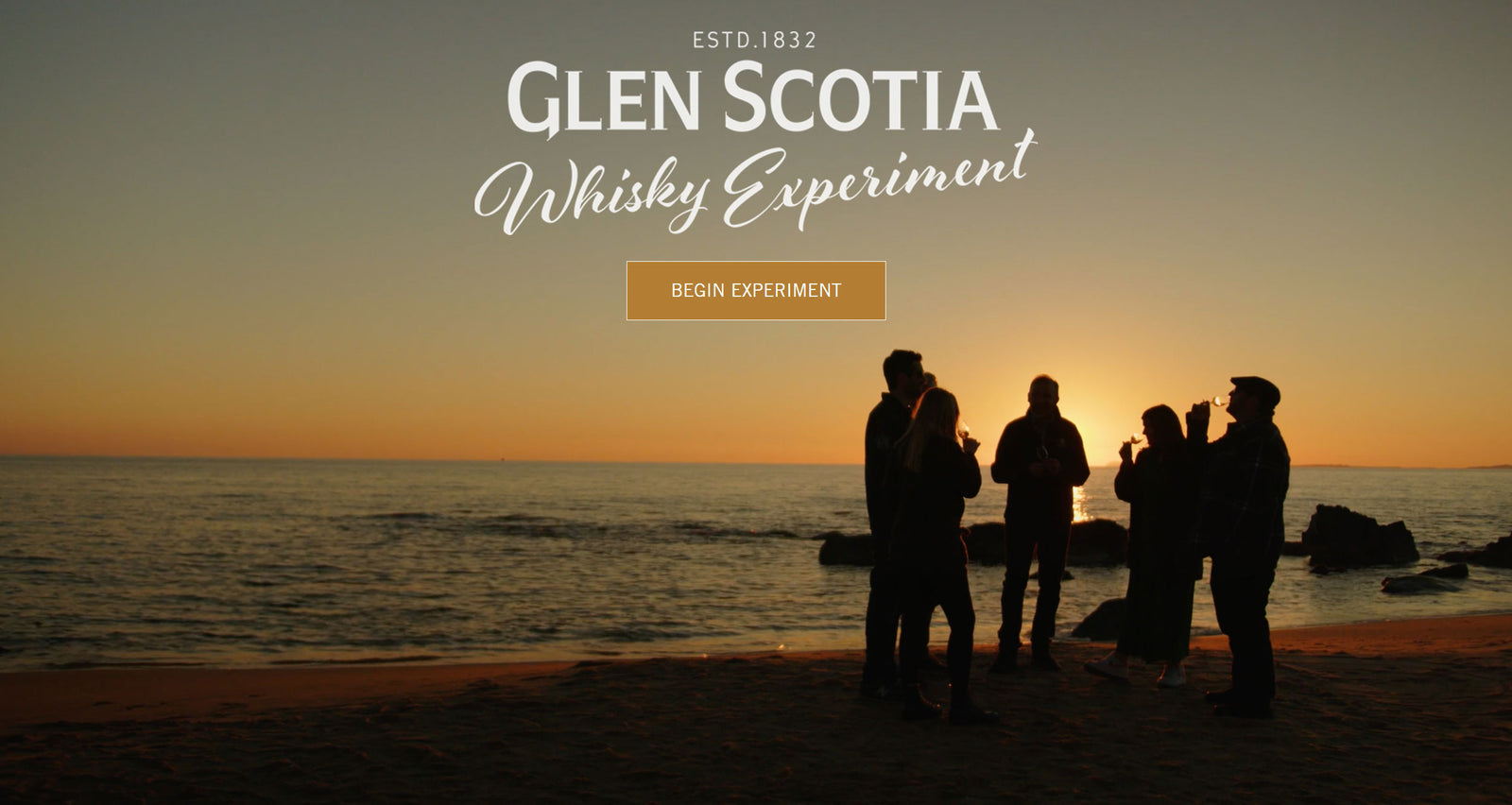 A group of people standing on a beach, silhouetted against a sunset. The scene is an advertisement for Glen Scotia Whisky Experiment, with a "Begin Experiment" button positioned in the center. "ESTD. 1832 GLEN SCOTIA Whisky Experiment" is written at the top of the image.